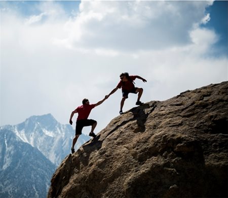 Two men helping each other climb up a mountain
